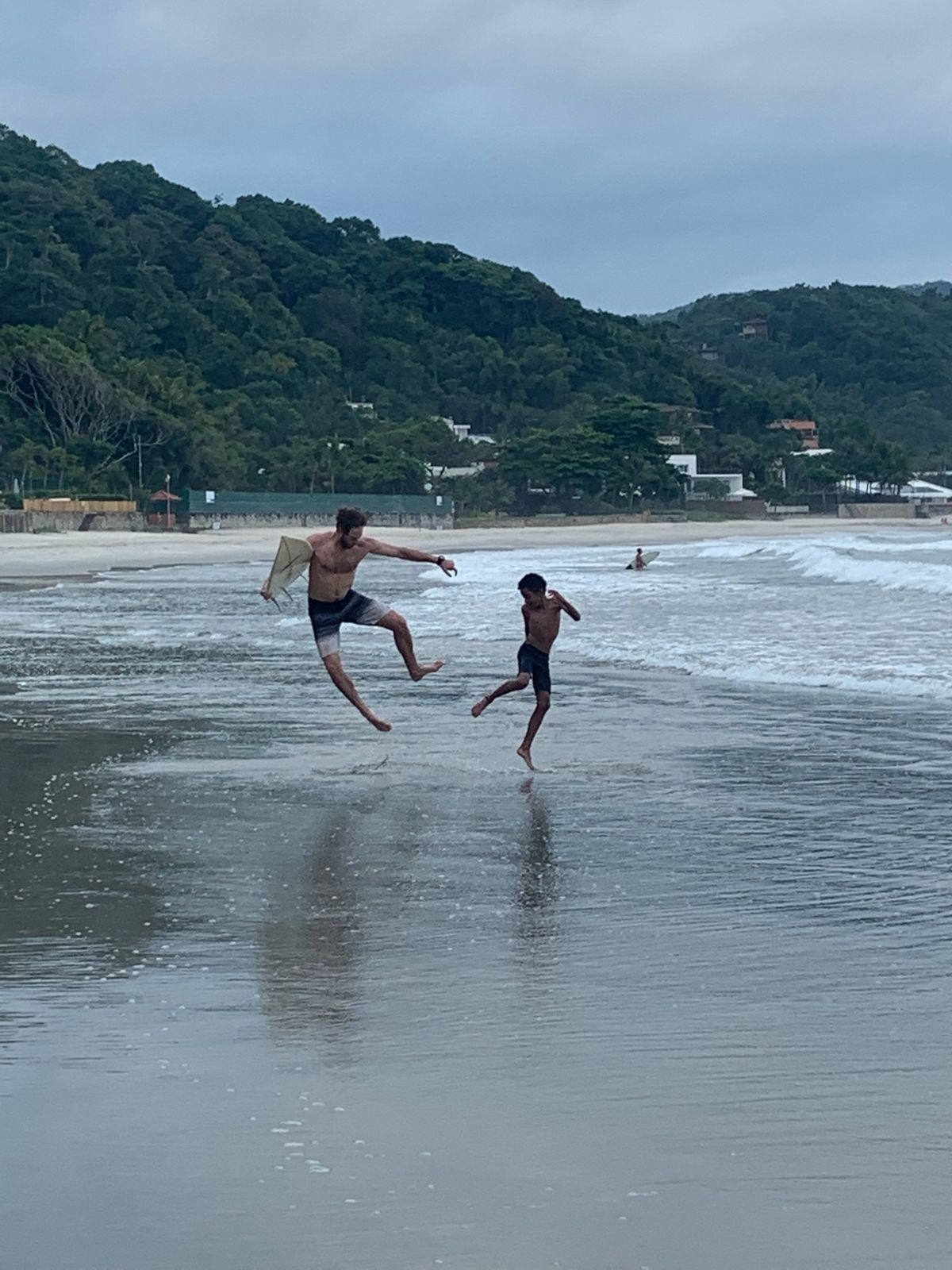 Nick and a young surfer leap in the shallows