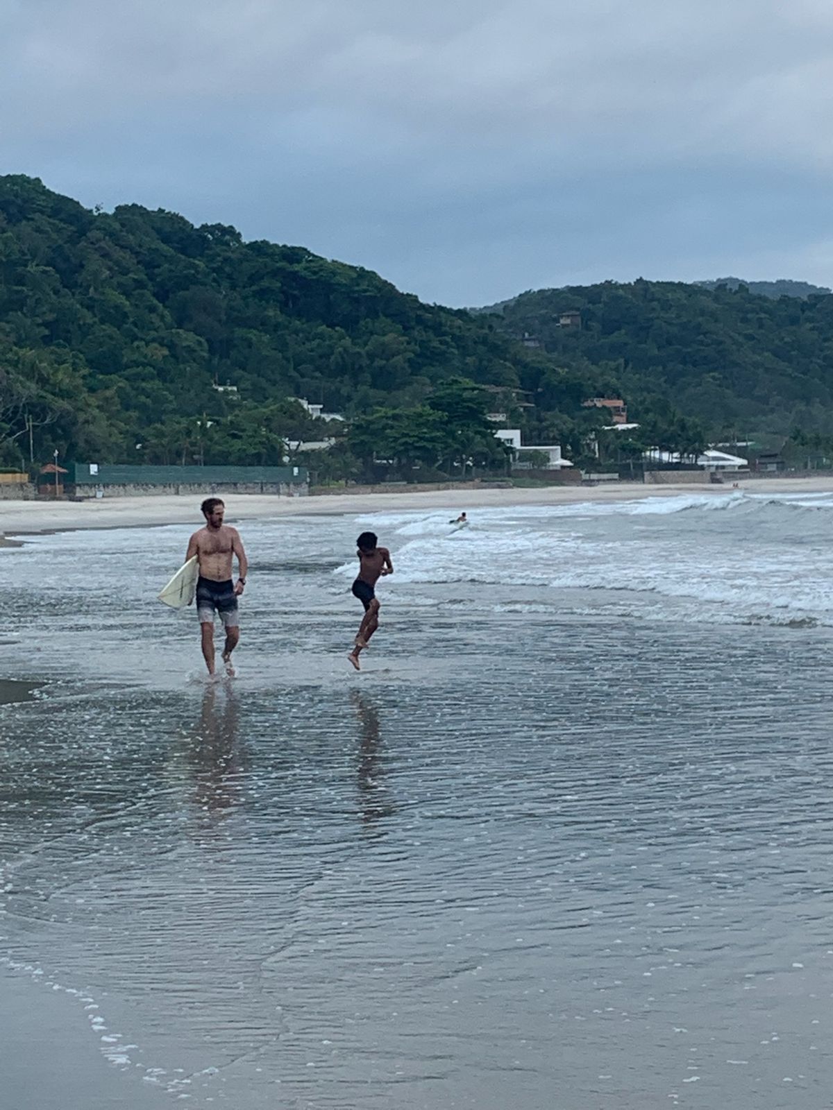 Nick walks out of the surf with his board as the boy runs ahead