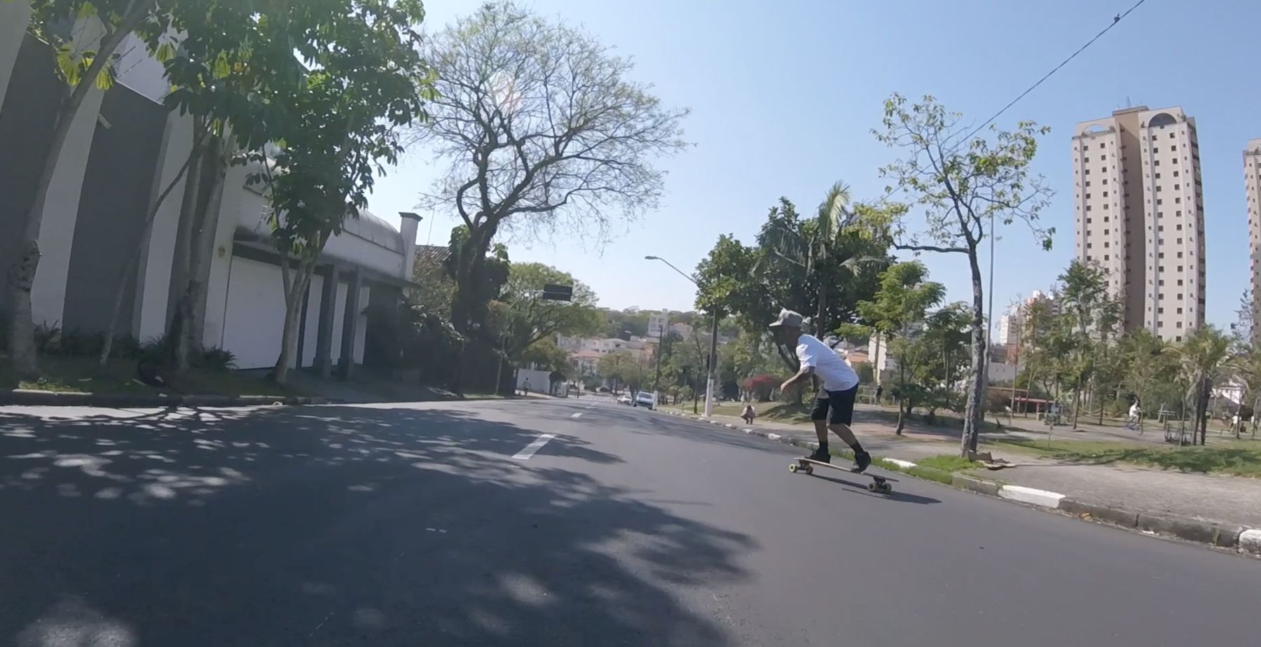 Marcelo longboards down a sunlit avenue past tower blocks