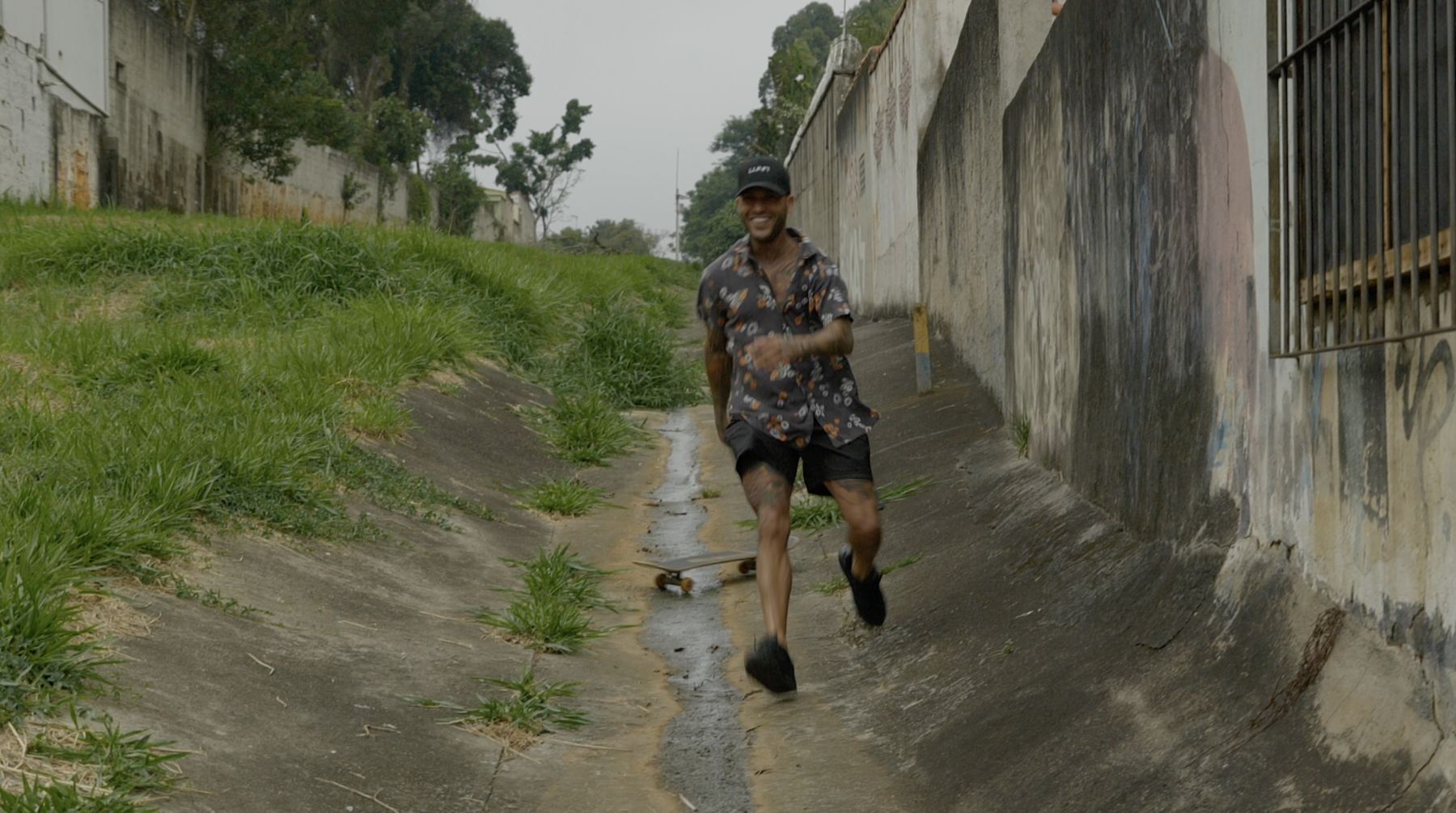 Marcelo runs laughing down the drainage channel after his board