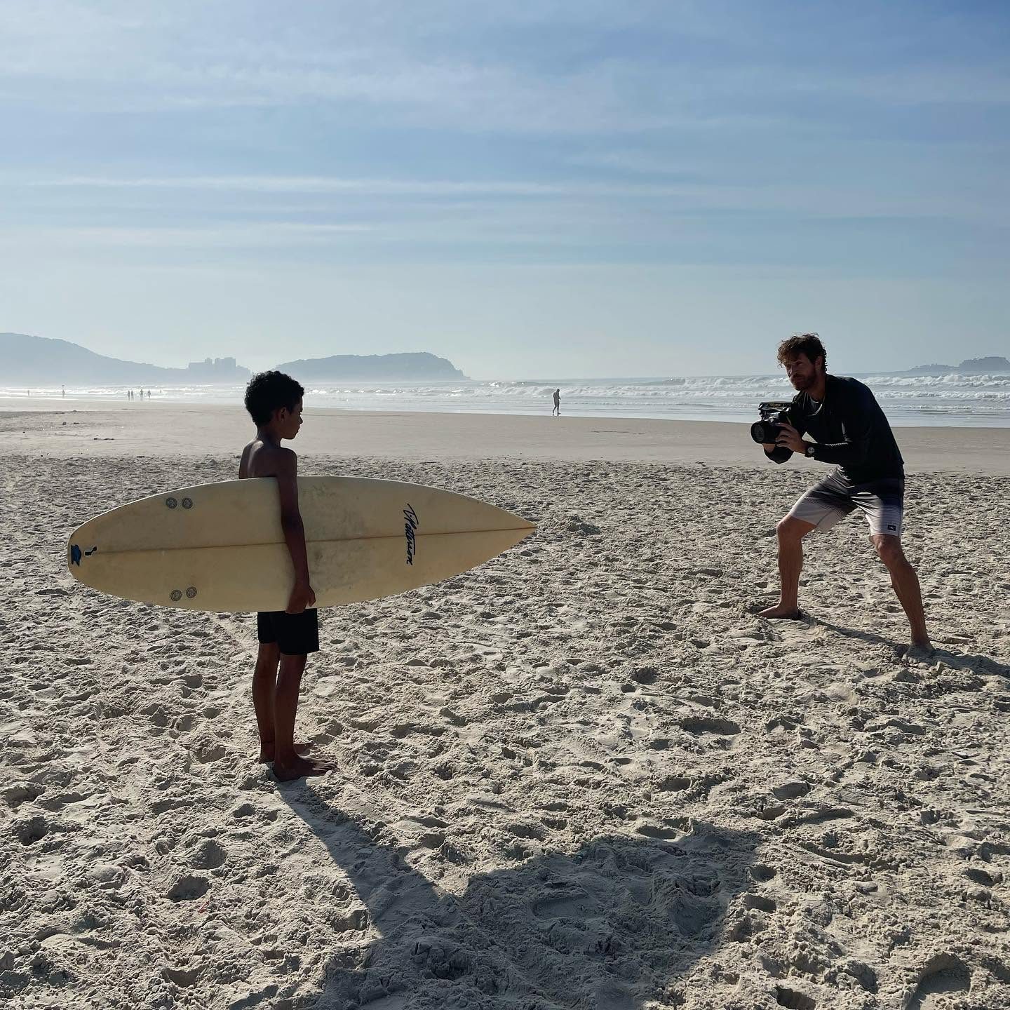 Nick photographs a young surfer holding his board on the beach