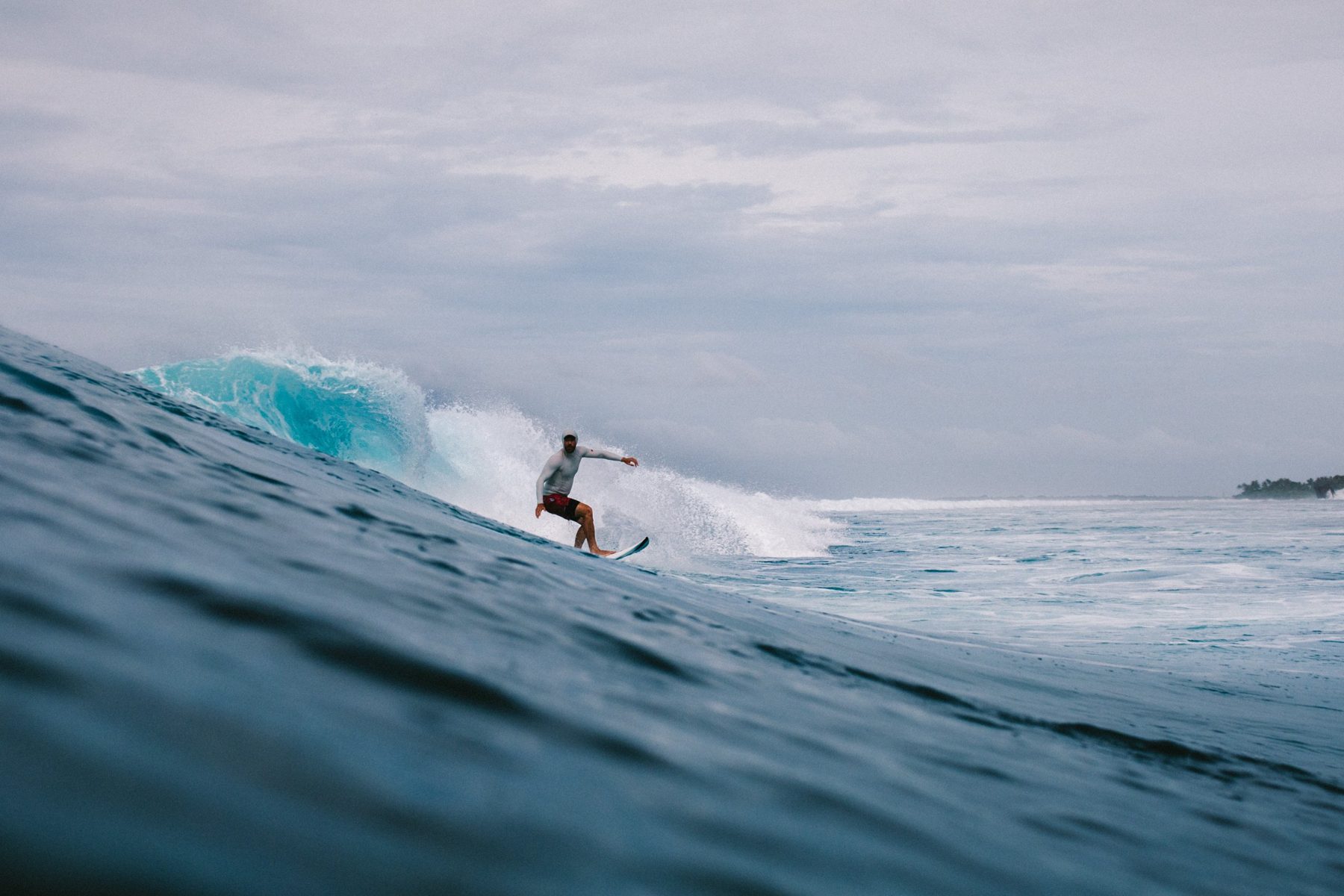 Nick carves a reef wave under a grey sky, shot from the water
