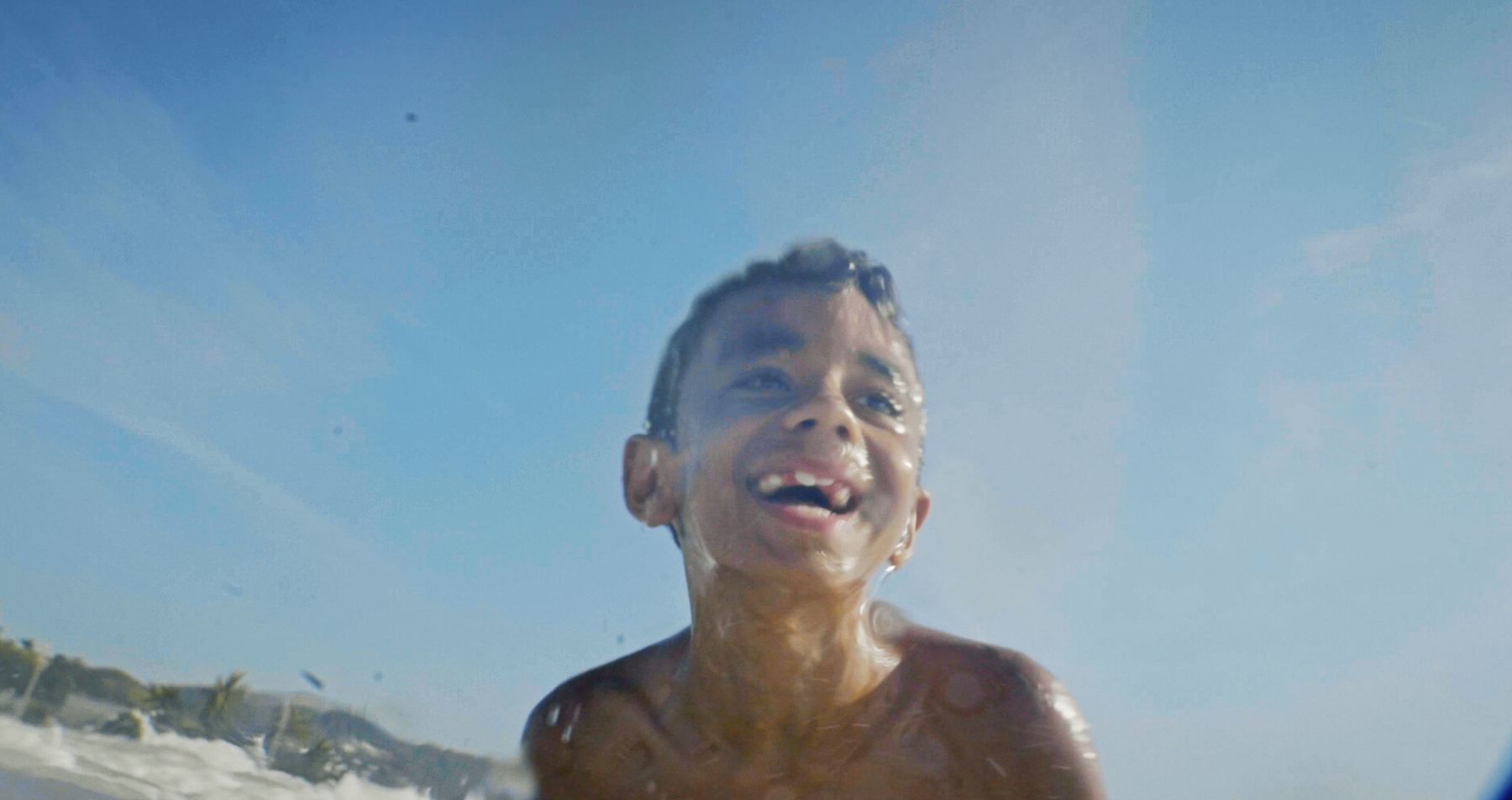 The boy grins up at a clear blue sky