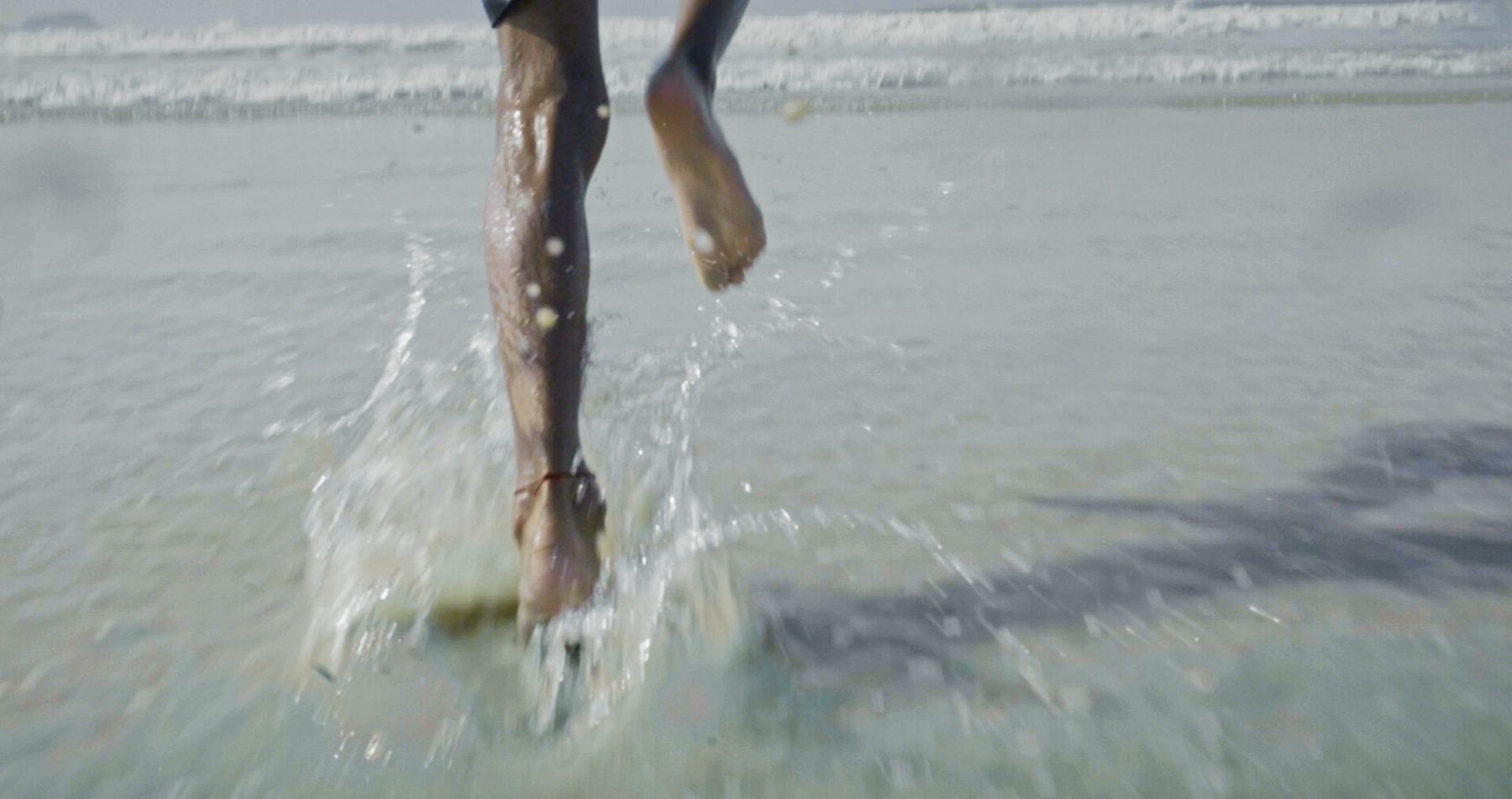 Bare feet splash through the shallows, running towards the sea