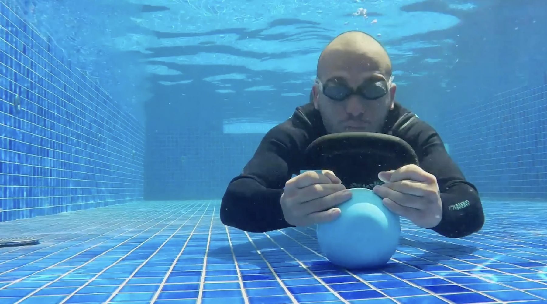 Marcelo trains underwater, holding a kettlebell on the floor of a pool