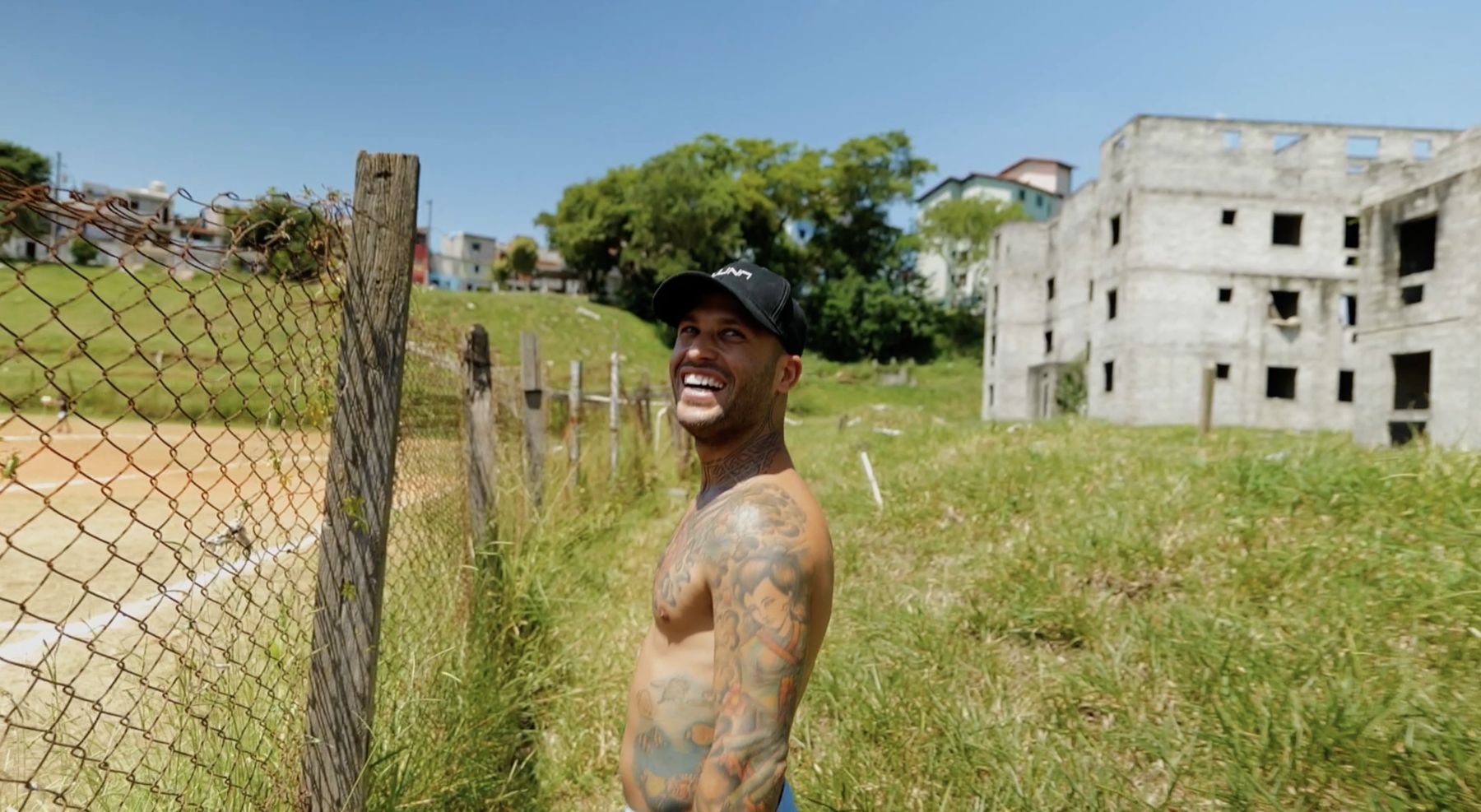 Marcelo laughs beside a chain-link fence and an unfinished building
