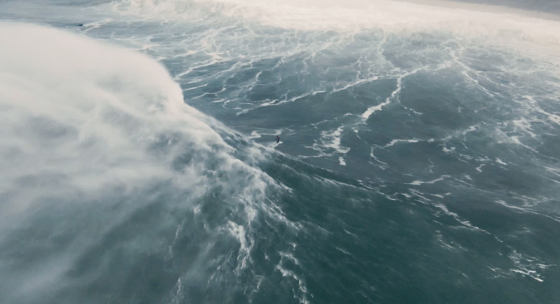 From above: a tiny figure in red races ahead of exploding whitewater