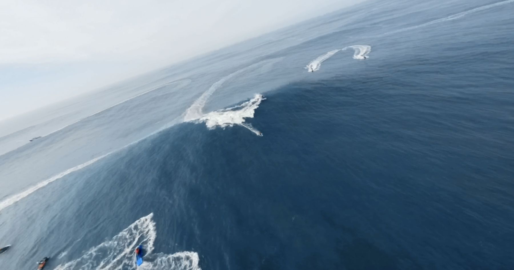 Overhead: jet skis carve circles around a breaking wave