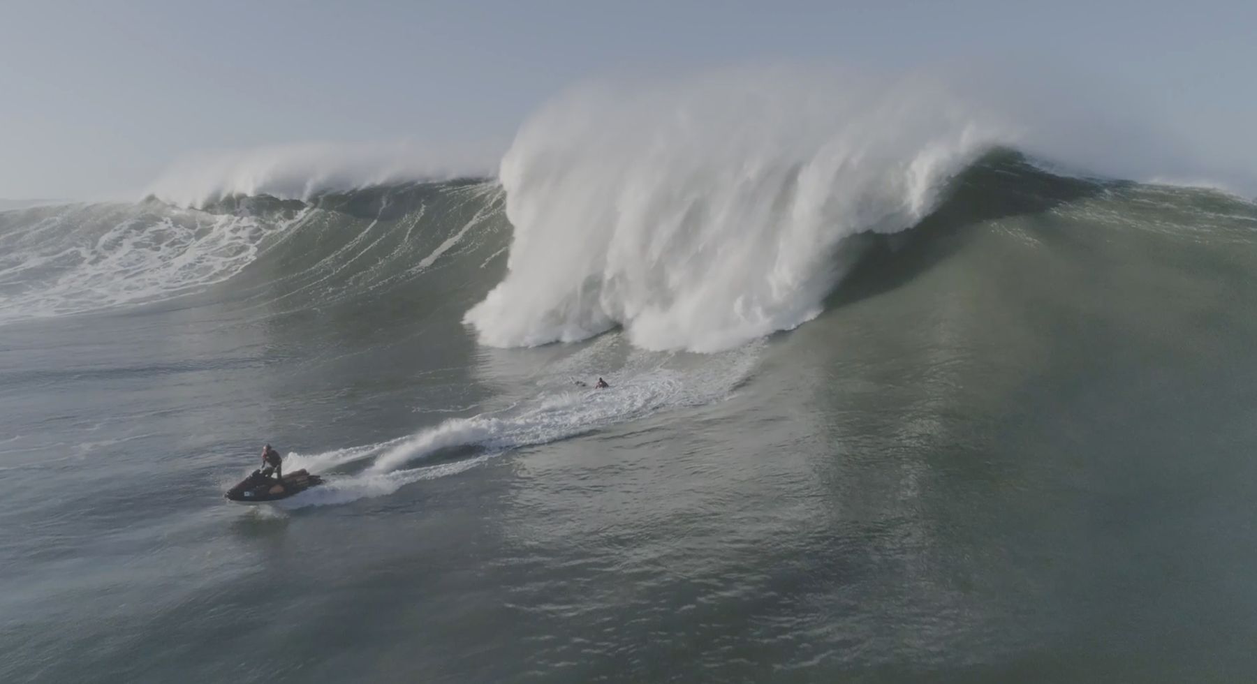 A jet ski races to pick up a surfer in front of collapsing whitewater