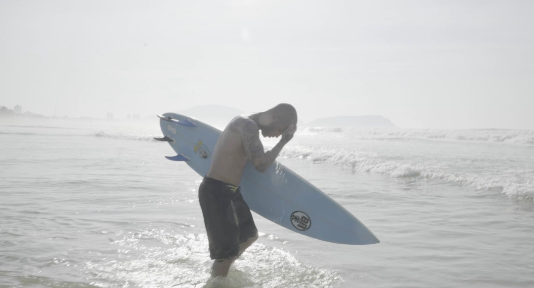 Marcelo wades out with his board, hand over his face