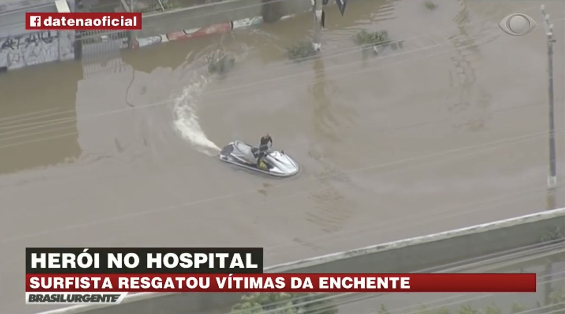 News helicopter footage: Marcelo pilots a jet ski through a flooded street. Caption reads: Surfista resgatou vítimas da enchente
