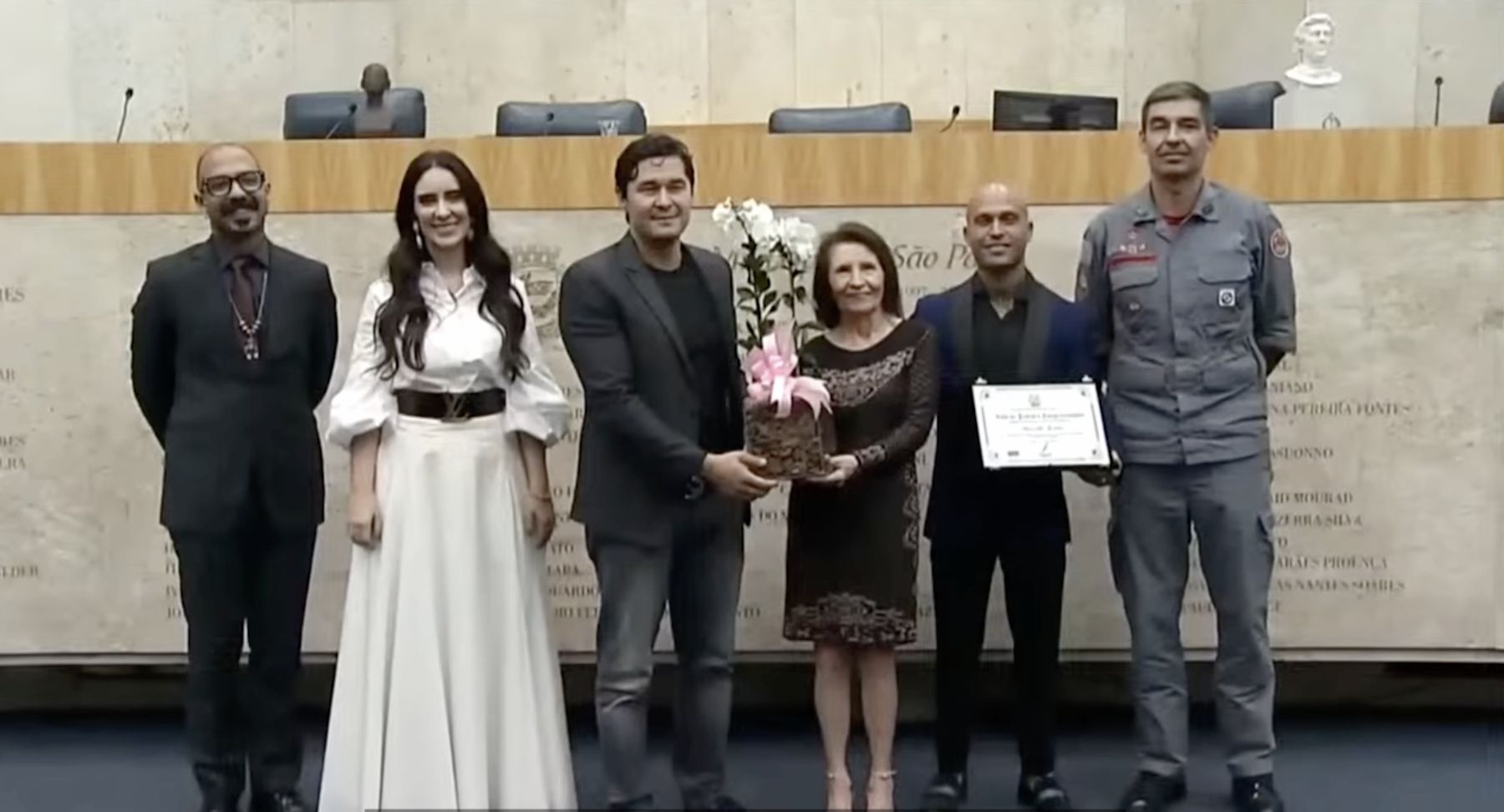 Marcelo receives a certificate at a civic ceremony in São Paulo, beside a firefighter